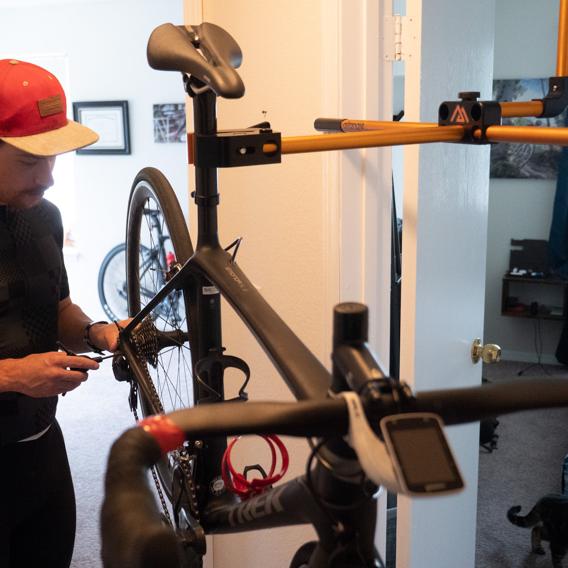 Man working on bicycle hanging from bike stand in doorway.